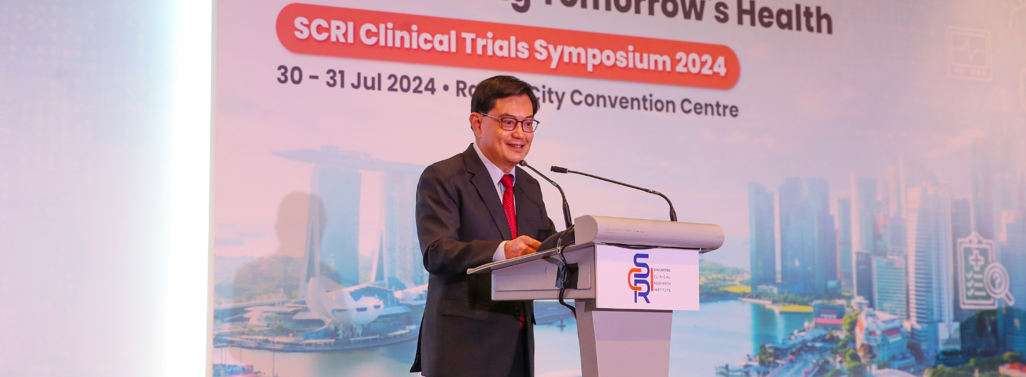 Speaker at SCRI Clinical Trials Symposium 2024 lectern, city backdrop.